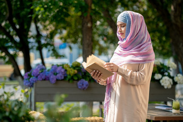 Casual young woman in hijab looking through book outdoors