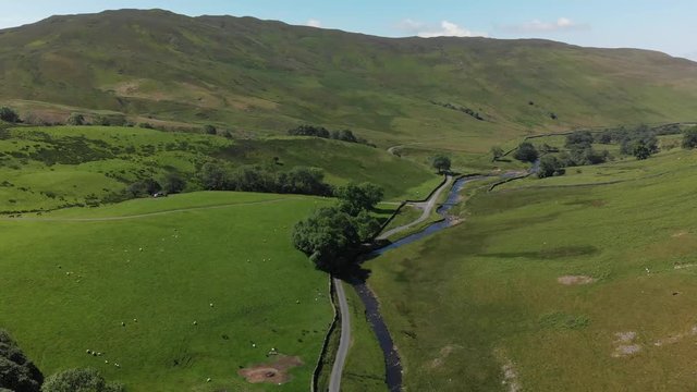 A descending aerial shot of Barbon Beck, Carnforth, Lancashire, England. This stunning countryside features a stream running alongside a small country lane.
