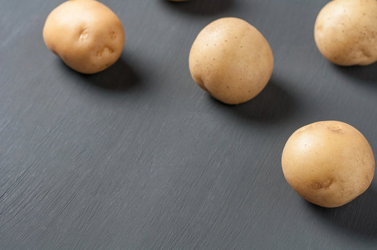 Scattered whole fresh ripe potatos lies on dark cement table. Copy space for text