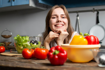 Obraz na płótnie Canvas young girl prepares a vegetarian salad in the kitchen, she sits at the table with food and dreams, the process of preparing healthy food
