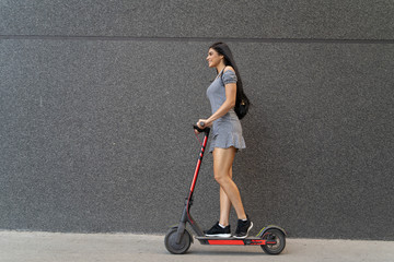 Side view beautiful long hair girl riding electric scooter, black wall background  © phoenix021