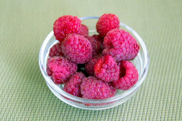 A small bowl of raspberries with a light green background.