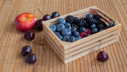 Still life with fruits. Raspberries, cherries, blueberries, blackberries and flat nectarines. In a small crate of a mat.
