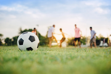 Action sport outdoors of kids having fun playing soccer football for exercise in community rural area under the twilight sunset sky. Fresh and vibrant image with anonymous people.