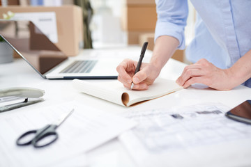 Female manager of online shop making notes on blank page of notebook