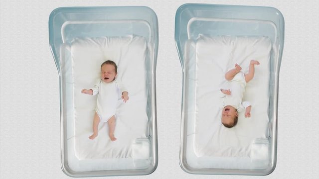 Two newborn children moving and crying in hospital cribs, twins baby brothers