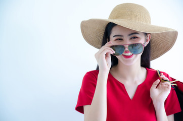 Young beautiful fashionable Asian woman holding shopping bags wearing red dress, sunglasses and hat over white background studio shot with smiling