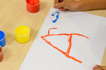 Girl painting on a white sheet with brush and colored paints: red, yellow, brown and blue....