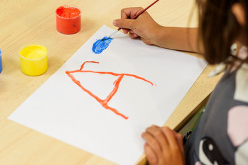 Girl painting on a white sheet with brush and colored paints: red, yellow, brown and blue....