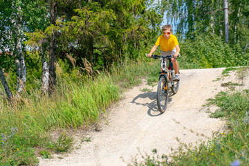 Fototapeta na wymiar The boy on the bike down the hill on a dirt road