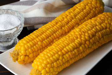 Boiled corn on a white plate on a dark wooden table. Close-up