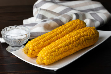 Boiled corn on a white plate on a dark wooden table. Close-up