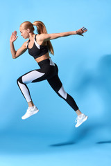 Fototapeta na wymiar fit strong fair-haired girl is running very fast, isolated blue background, studio shot. interest, hobby, lifestyle. long jump. fitness