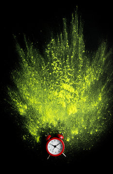 Red alarm clock with yellow holi powder explosion on black