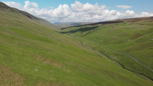 A high-altitude aerial shot of Barbon Beck, Carnforth, Lancashire, England. Slowly flying into the valley, this stunning countryside features a stream running alongside a small country lane.
