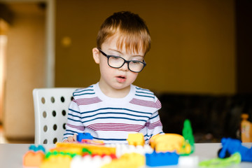 little boy in the glasses with syndrome dawn playing with colorful bricks
