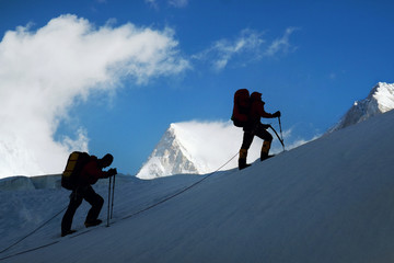 Climber belays team member on summit ascend of mountain peak. Success, freedom and happiness,...