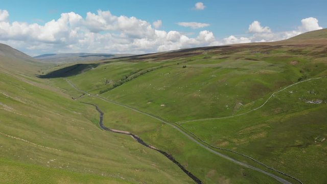 A high-altitude aerial shot of Barbon Beck, Carnforth, Lancashire, England. This stunning countryside features a stream running alongside a small country lane.