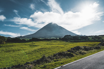Fototapeta premium Straight EN3 longitudinal road northeast of Mount Pico and the silhouette of the Mount Pico along , Pico island, Azores, Portugal.