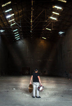 Drummer Man Holding Drum And Cymbal In Dark Abandoned Warehouse Full Of Debris. Preparing Music Party Or Rave In Abandoned Place With Beautiful Light..