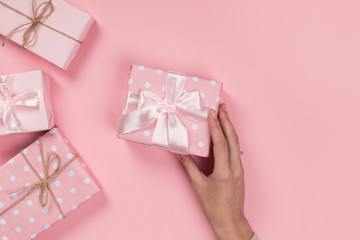 Womans hands holding gift or present box on pink pastel table top view. Flat lay composition for birthday or New Year.