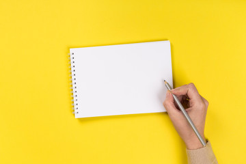 Woman's hands with perfect manicure holding pencil and  notepad as mockup for your design. Yellow background, flat lay style.