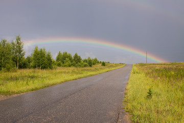 The road going to the horizon and a big rainbow in the sky