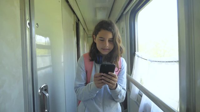 teen girl walks on a train compartment car with a backpack and a smartphone. travel transportation railroad concept. the girl in the train at the window corresponds the girl in the train wagon at the