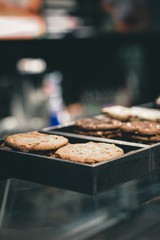 Cookies in the box over the coffee store menu board. Stands with tasty sweets on table in cafe. Background of different dessert cakes for sale