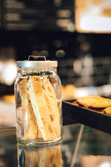 Cookies in the jarr and in the box over the coffee store menu board. Stands with tasty sweets on table in cafe. Background of different dessert cakes for sale