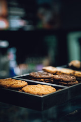 Cookies in the box over the coffee store menu board. Stands with tasty sweets on table in cafe. Background of different dessert cakes for sale