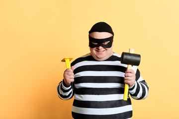 plump thief with hammer standing isolated on yellow background, close up portrait