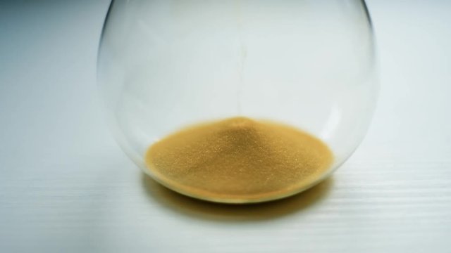Glass sandwatch with yellow sand on white table. Time and life concept. UHD 4K video