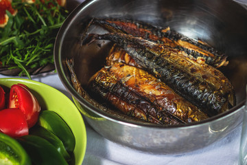 grilled fish, mackerel in a large metal bowl and vegetables with arugula, close-up