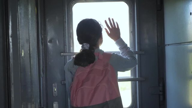 little teenage girl is a backpacker traveling lifestyle by train. travel transportation railroad concept. tourist school girl in the train wagon with backpack looking out the window waving his hand