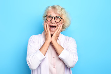 senior emotional doctor woman terrified with fear, shouting in shock. Panic concept.woman in glasses with wide open mouth expresses fear, surprise. isolated blue background. studio shot.