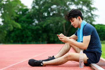 Young Asian athletic man sitting and listening music from mobile phone to relax during rest