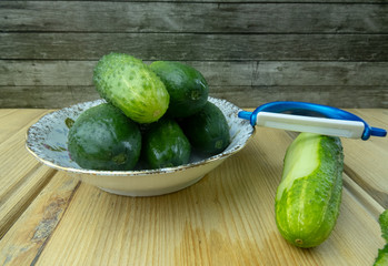 Green cucumbers on a plate on the table. Nearby lies a vegetable peeler slicer.