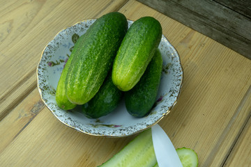 Green cucumbers on a plate on the table. Nearby lies a cucumber cut in half and a knife. Two cucumber slices.