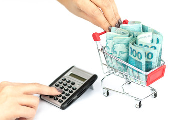 Female hand puching brazilian notes one hundred (100) reais, shopping cart or supermarket trolley and calculator and calculator, business finance shopping concept. Brazil money. © Gabriel Ramos