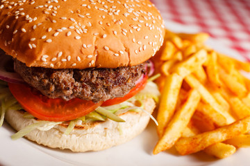 Tasty burger in the restaurant. Sesame bun, meat Patty, tomato, lettuce and pickle. Served with French fries