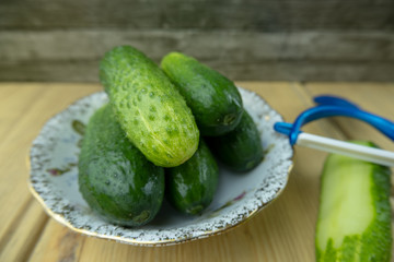 Green cucumbers on a plate on the table. Nearby lies a vegetable peeler slicer.