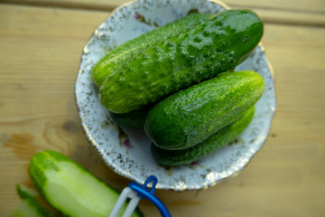 Green cucumbers on a plate on the table. Nearby lies a vegetable peeler slicer.