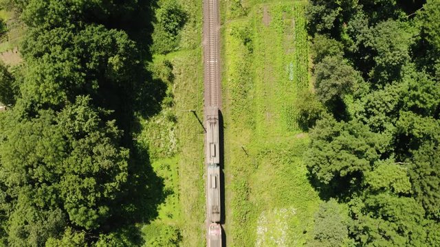 Train moving on railroad through green summer forest. Aerial drone view. UHD 4K video