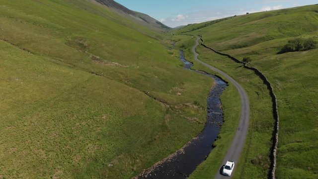 An aerial shot of Barbon Beck, Carnforth, Lancashire, England. This stunning countryside features a stream running alongside a small country lane with a car travelling by.