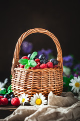 Fototapeta na wymiar Raspberries and blueberries in a basket with chamomile and leaves on a dark background. Summer and healthy food concept. Selective focus. Background with copy space.