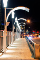 Contemporary lamps with concave shape lines the sidewalk across the city street bridge in early...