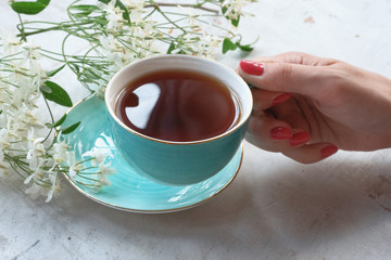 Woman is holding a cup of hot tea on a white wooden table background.