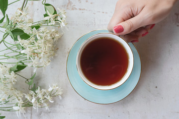 Cup of hot tea in a female hand on a white wooden table background.