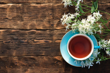 Cup of hot tea and blooming white flowers on a brown wooden table flat lay background.